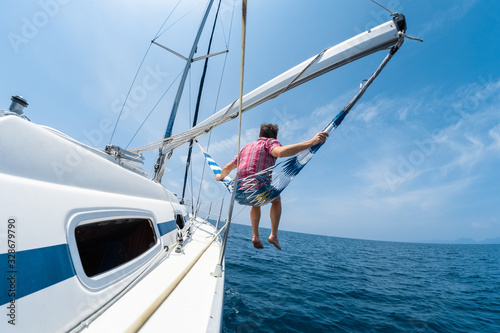 Young man enjoys tropical sailing in the hammock set on the boom of the yacht
