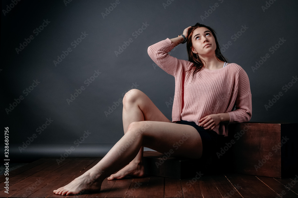 Beautiful sporty young girl model posing on a gray background. Woman in sportswear shorts and a white top and in a pink sweater, touches her hair and looks up Beautiful sporty young girl model posing on a gray background. Woman in sportswear shorts and a white top and in a pink sweater, touches her hair and looks up