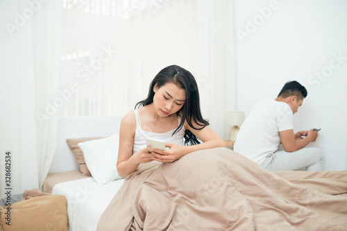 sad view of young married couple using their mobile phone in bed ignoring each other as strangers in relationship and communication problems © makistock