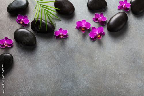 Spa composition with flowers, green leaves and massage stone on gray background top view. Beauty treatment and relaxation concept. Flat lay. .