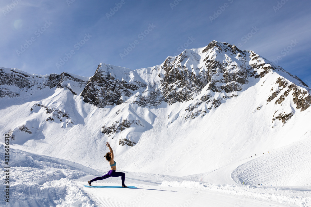 A young woman practice yoga in mountains. With a great view of snow and winter landscape.