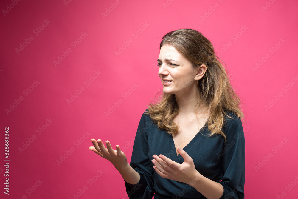 Portrait of a beautiful girl looks aside with pensive expression, is considering a plan for further action on a pink background.