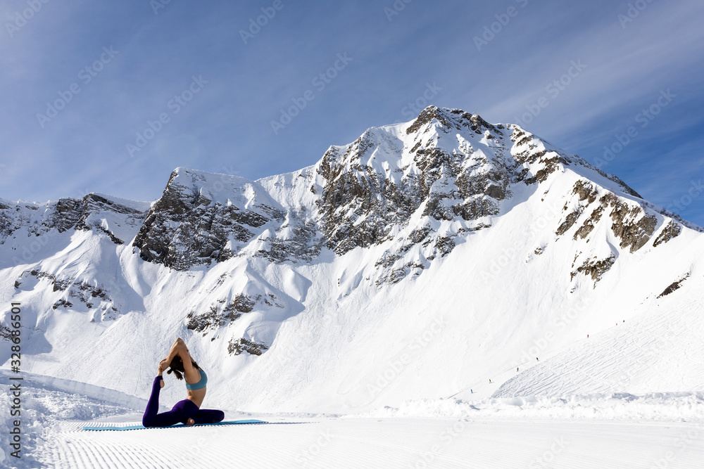 A young woman practice yoga in mountains. With a great view of snow and winter landscape.