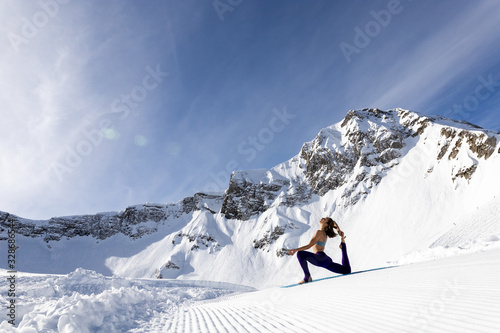 A young woman practice yoga in mountains. With a great view of snow and winter landscape.