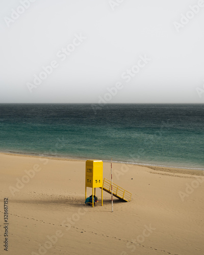 Very calm shot of beach with textured sand hills, blue water and yellow rescue post © tavi004