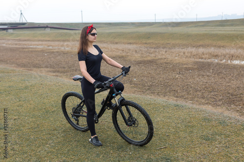 Girl on a mountain bike on offroad, beautiful portrait of a cyclist at sunset, Fitness girl rides a modern carbon fiber mountain bike in sportswear. Close-up portrait of a girl in a helmet and glasses