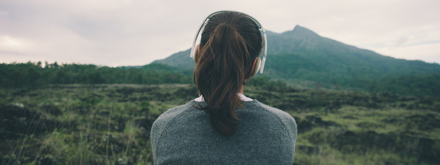 Woman in headphones listening music in nature and at the mountain