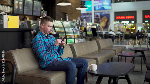 A young man is sitting in a cafe with a phone. The man is in correspondence on a smartphone. Close-up.