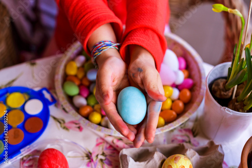 Little girl holding a bright colored Easter egg in her hands. Happy Easter Sunday celebration. Copy space