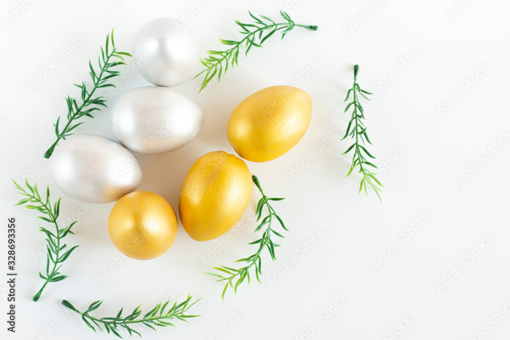 Gold and silver eggs, green sprigs of plants on a white-yellow background. Minimalistic composition. Easter holiday card. Gold and silver eggs, green sprigs of plants on a white-yellow background. Minimalistic composition. Easter holiday card.
