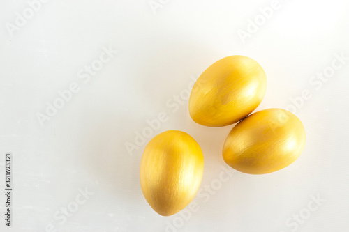 Three eggs of gold color on a white background. Minimalistic composition. Easter holiday card.