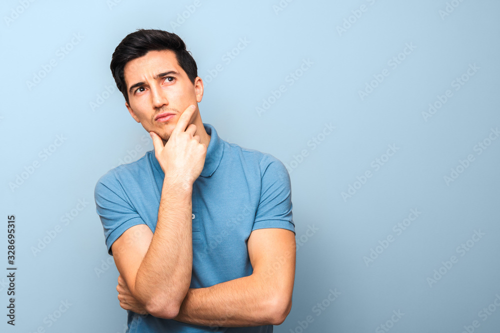 what can I do. pensive man in blue polo shirt against a blue background with hand on his chin and looking up with copy space what can I do. pensive man in blue polo shirt against a blue background with hand on his chin and looking up with copy space