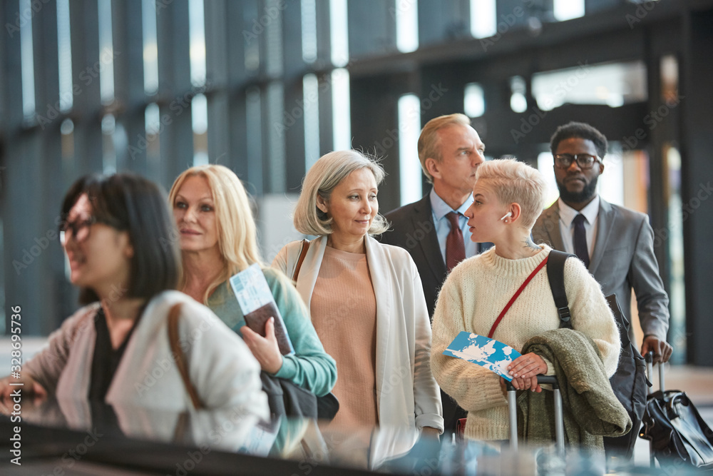 Two women chatting while standing in airport customs queue, horizontal medium portrait, copy space