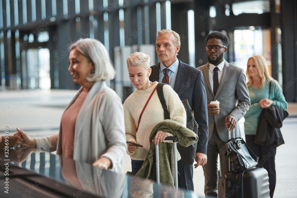 Fototapeta premium Group of people standing in queue at airport check-in counter desk, horizontal medium shot, copy space