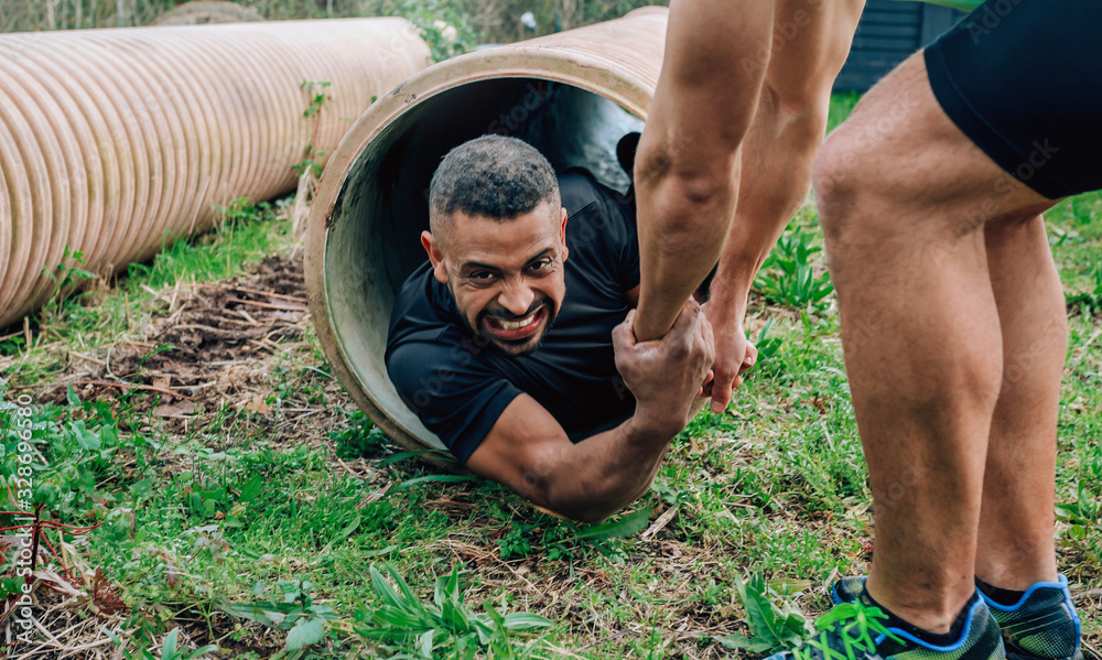 Male participants in an obstacle course going through a pipe - obrazy, fototapety, plakaty 