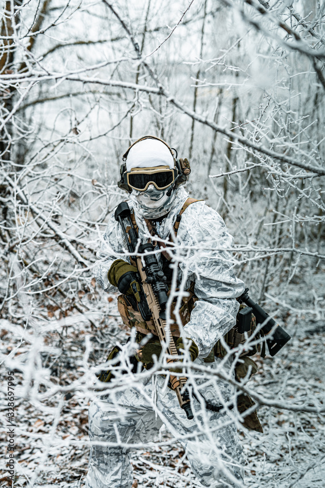 Airsoft man in white camouflage uniform and machinegun with optical sight. Soldier in the winter forest between branches. Vertical photo.