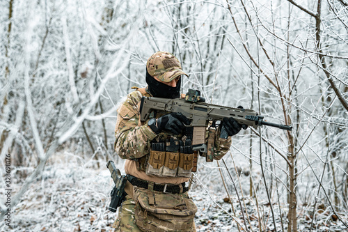 Airsoft man in camouflage uniform and machinegun with optical sight. Soldier in the winter forest. Horizontal photo.