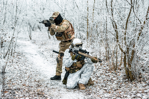 Two airsoft man in camouflage white green uniform back to back with machinegun. Soldier in the winter forest. Horizontal photo.