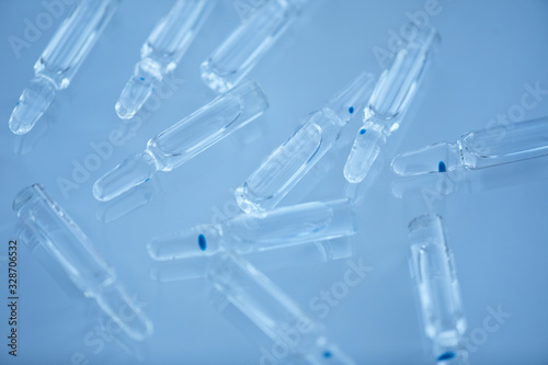 Horizontal close up high angle view shot of ampoules with transparent liquid medication lying on light blue surface