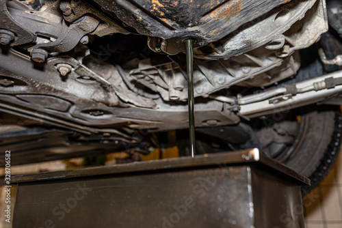Draining used diesel engine oil from an oil pan into a metal container in a car workshop.