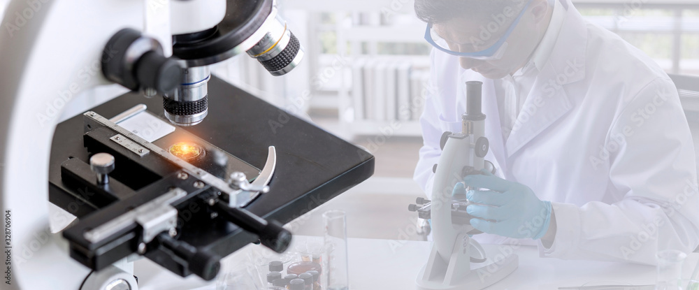 Laboratory concept; close up of microscope with a blurred picture of the scientist is researching in laboratory Laboratory concept; close up of microscope with a blurred picture of the scientist is researching in laboratory