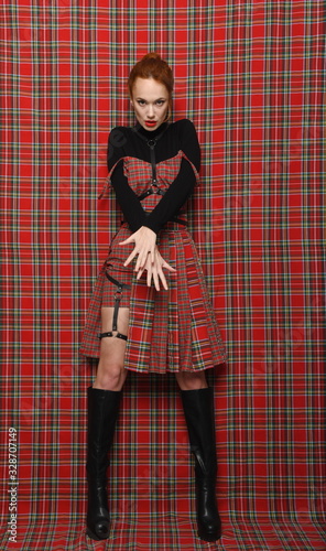 Modern fashion. A girl in a plaid (checkered) dress on a plaid background in black golf with a bare leg demonstrates a modern stylish fashionable pose.