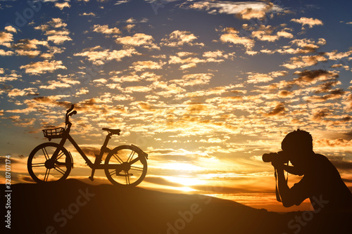 Silhouette of photographer taking pictures a bicycle at sunset background.