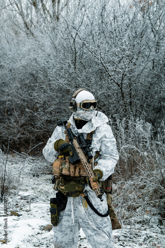 Fototapeta premium Military man in white camouflage uniform with machinegun. Soldier in the winter forest territory background