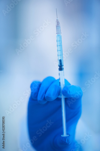 Woman's hand in blue disposable latex glive holding syringe full of new vaccine, vertical close up shot