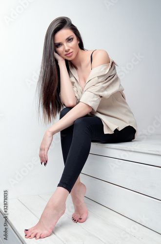 Studio fashion shot of cute young woman. Portrait of beautiful girl dressed in jeans and shirt. Seductive lady sitting on stairs
