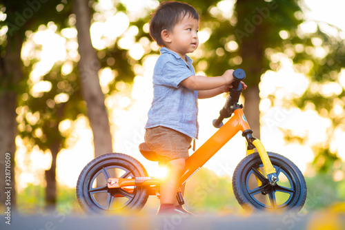 Fototapeta Naklejka Na Ścianę i Meble -  Baby 1-2 year old boy ride balance bike on road in park sunset light