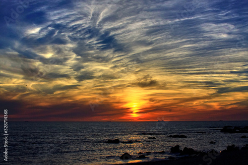 View of the orange sunset on the sea from a rocky beach