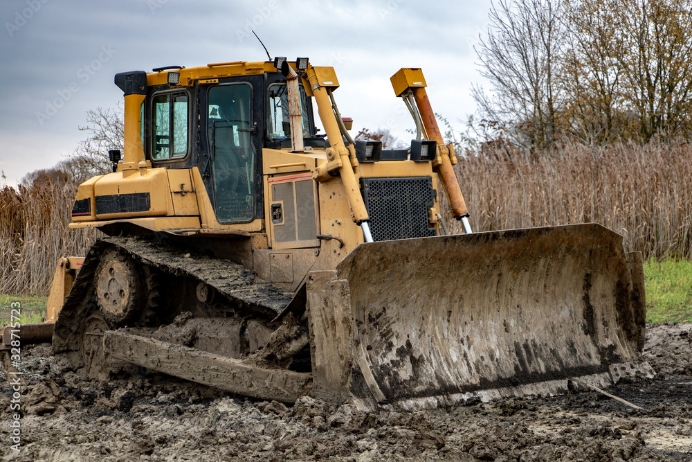 Dirty bulldozer standing in the mud. Autumn construction site with working machines.