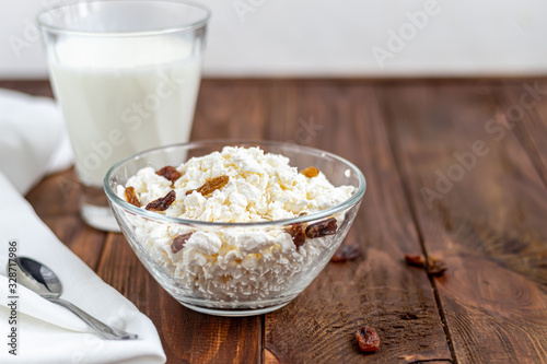 Fresh cottage cheese in a transparent bowl with raisins. In the background is a glass of kefir. Fermented foods. Good bacteria for health. Wood background.