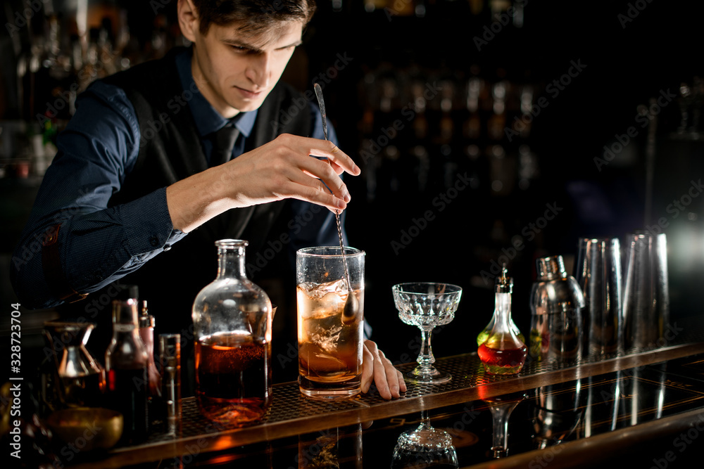 Young bartender gently stirs cold cocktail with spoon