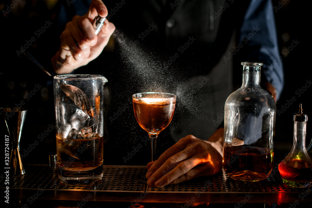 Close-up how barman sprinkles on a glass with a brown alcoholic drink.