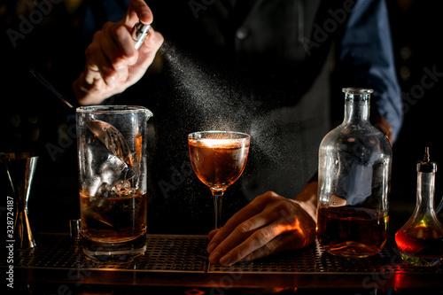 Close-up how barman sprinkles on a glass with a brown alcoholic drink.