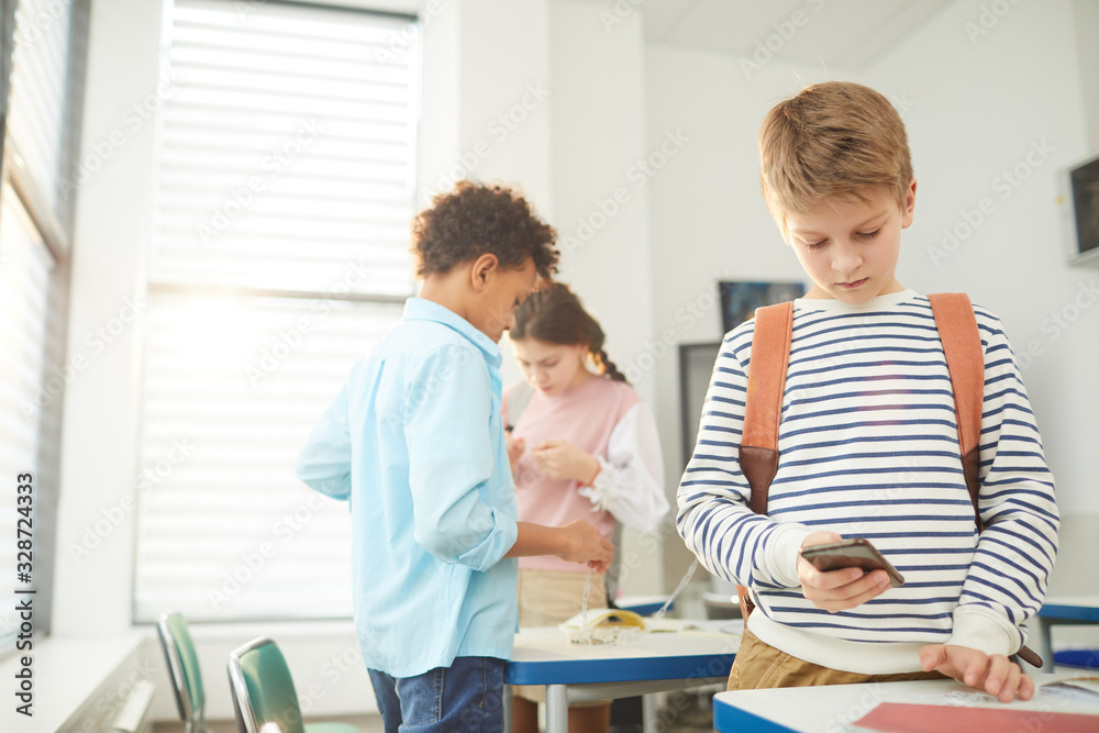 Middle school students standing in classroom using their smart phones during break, copy space