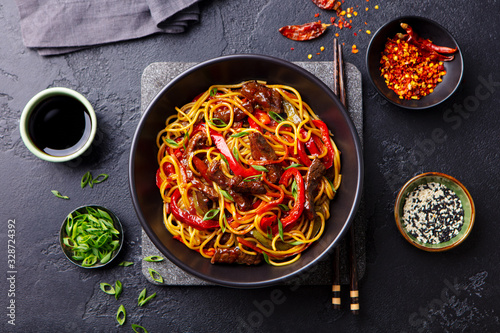 Stir fry noodles with vegetables and beef in black bowl. Slate background. Top view. photo