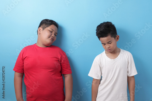Two Asian boys student tired and sleepy while standing against blue background