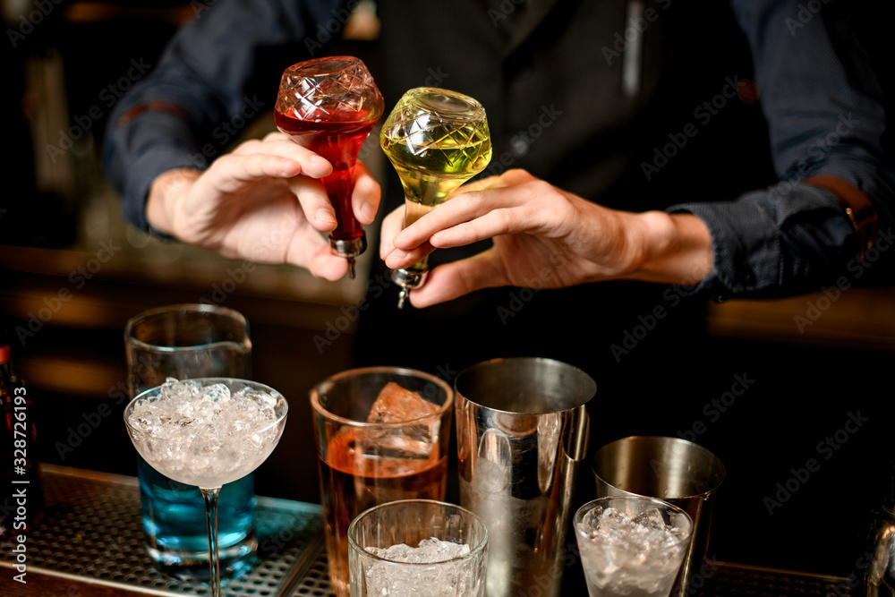 Barman holds bottles with necessary ingredients for making cocktail