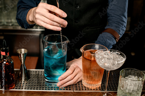 Close-up of bartender stirring blue cocktail in glass with spoon.
