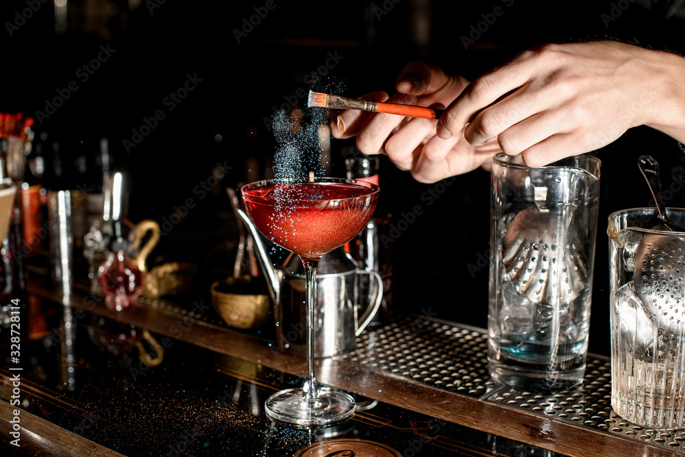 Barman carefully add seasoning to red cocktail in wineglass.