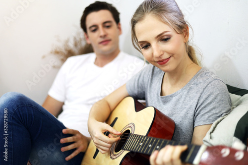 Young couple lover playing acoustic guitar on bedroom at home.