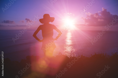 Silhouette of a woman with tropical sunset above the ocean.