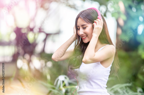 Happy young beautiful girl listening to the music with her pink headphones and dancing in the urban park 