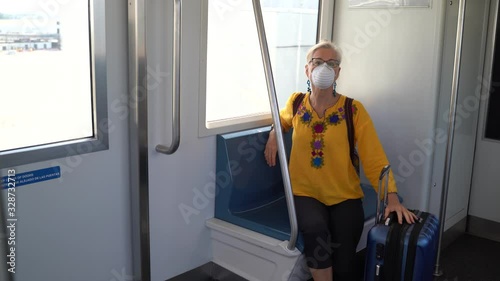 Woman wearing protective breathing mask looks out a moving train window with luggage at an airport. photo