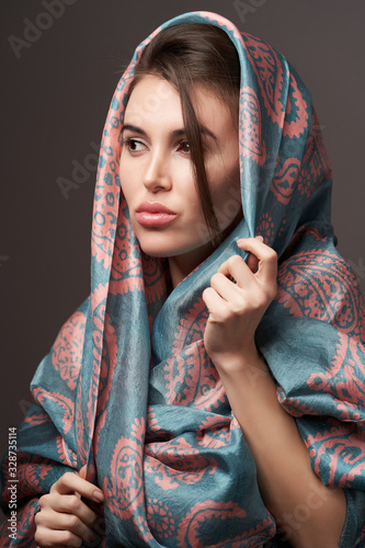 Beautiful young woman portrait with silk scarf on gray background