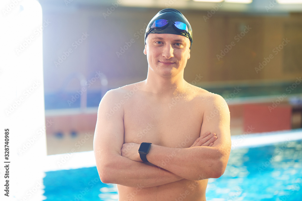 Close up portrait of sporty muscular man in swimming goggles and cap with a naked torso on background of swimming pool indoors