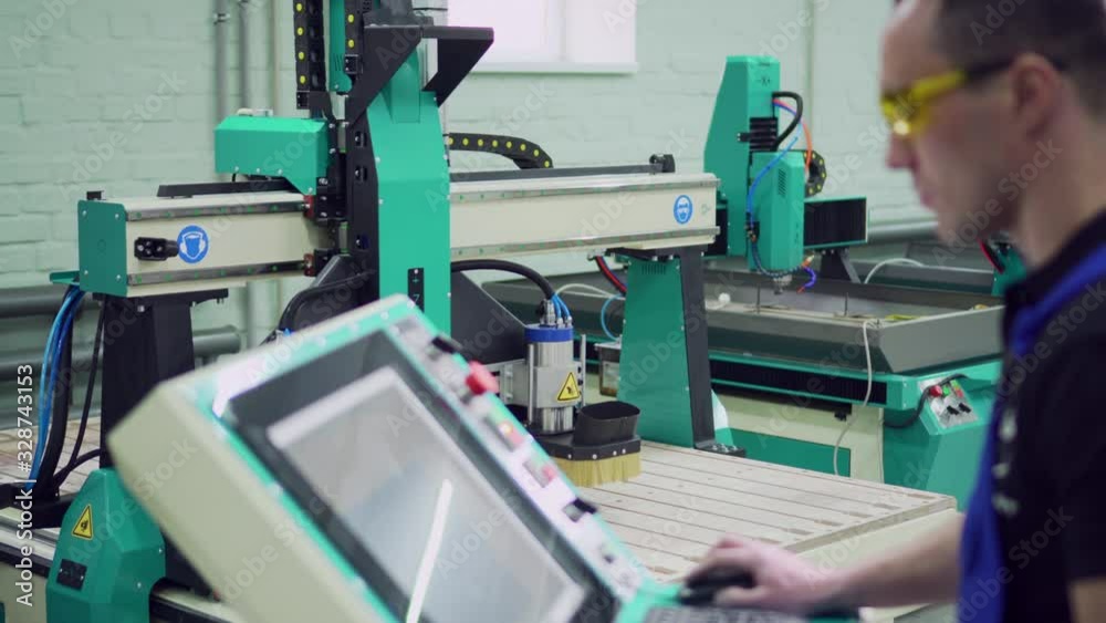 A male operator controls the CNC machine while standing at the control panel. Selective focus.